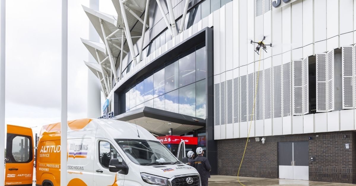 A specialized drone performing aerial pressure washing on a large commercial building facade.